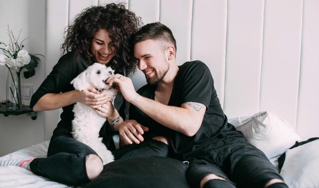 We love our furry friends a man and woman sitting on a bed playing with a dog